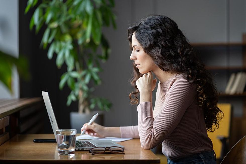 Woman on laptop works on her time management skills by writing down her priorities