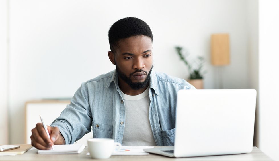 Job seeker on laptop writes notes as he views openings through various job board websites