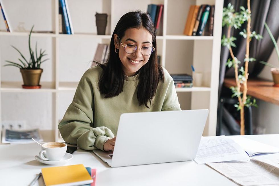 Happy young woman on her laptop writes for a blog while looking for a job