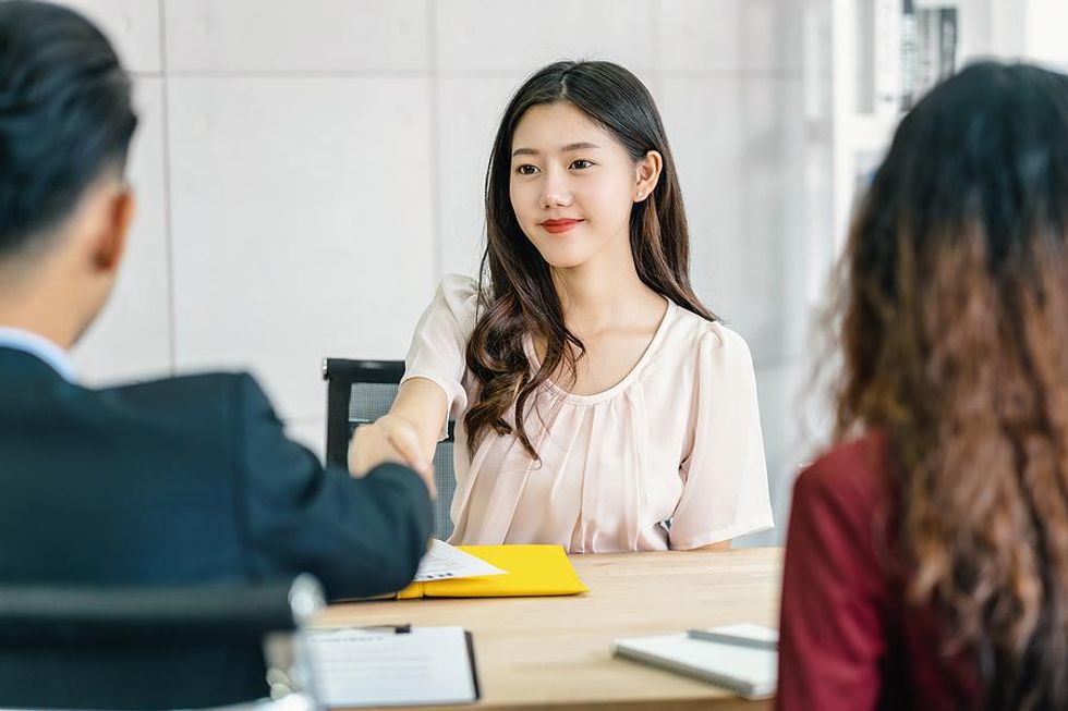 Woman shaking hands is asked, "Why should we hire you?" in a job interview